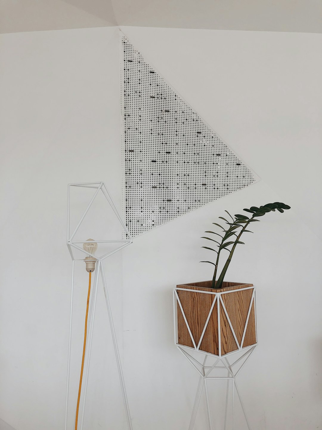 Eine Zimmerpflanze in einem Holzübertopf neben einer geometrischen Lampe.