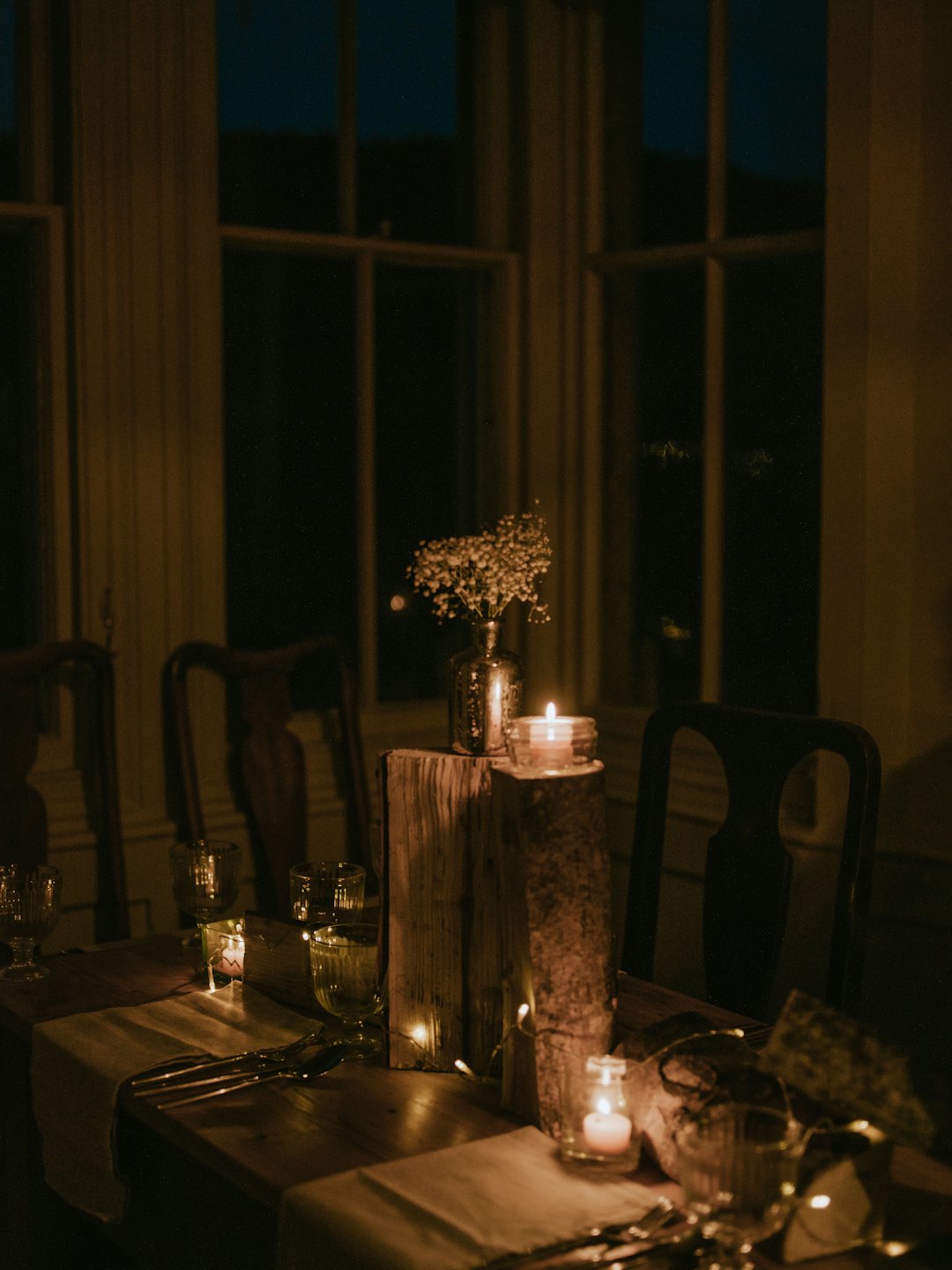 Esstisch mit Kerzen und Blumen in der Nähe von großen Fenstern.